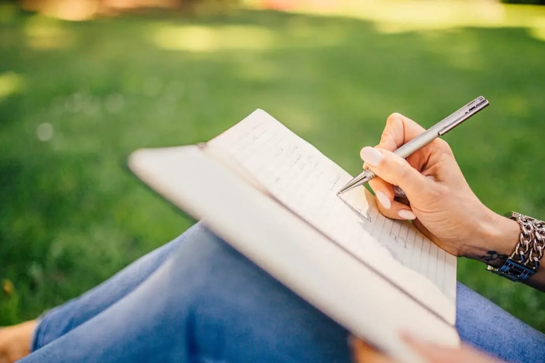 Mãos escrevendo em um caderno ao ar livre